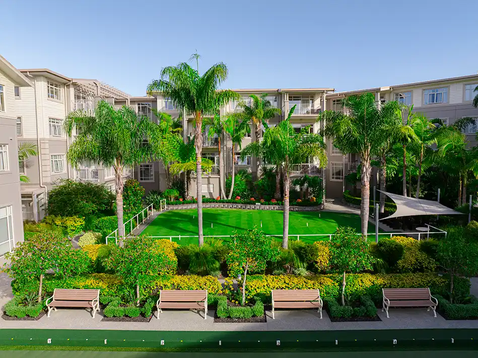 Lush central courtyard at Settlers Lifestyle Village, featuring a well-maintained bowling green, tropical landscaping, palm trees, and surrounding apartment buildings with balconies